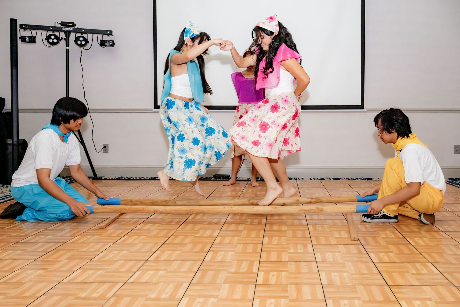 Children perform a traditional folk dance on a wooden floor stage during a cultural event.