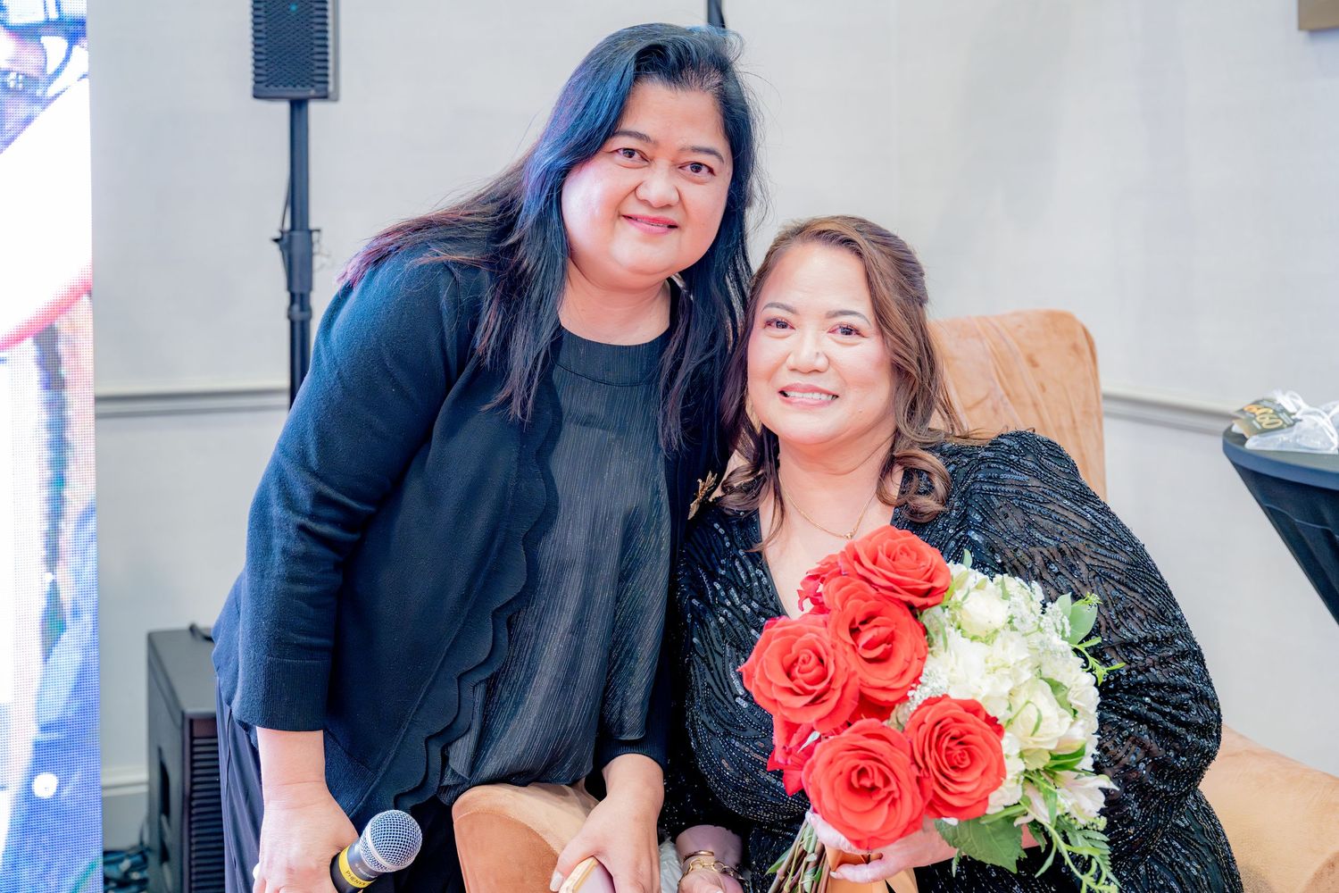 Two women posing together, one holding red roses bouquet at a milestone birthday party.