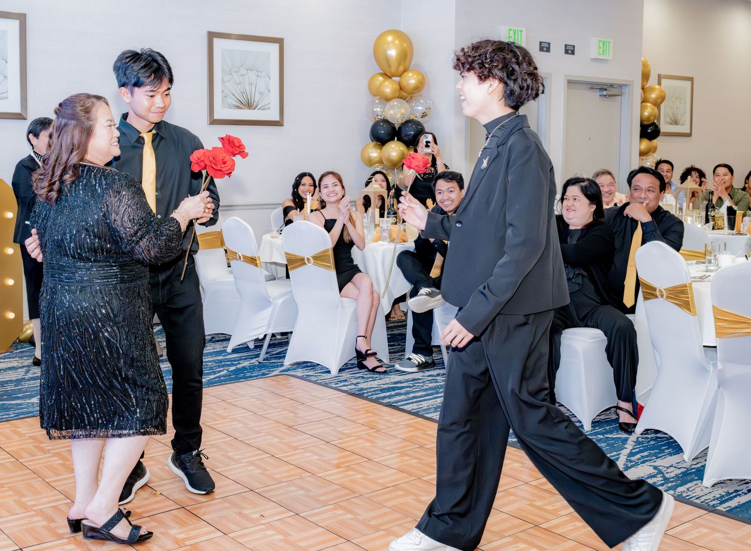 Two young men approach woman in black sequin dress on dance floor at formal birthday party event.