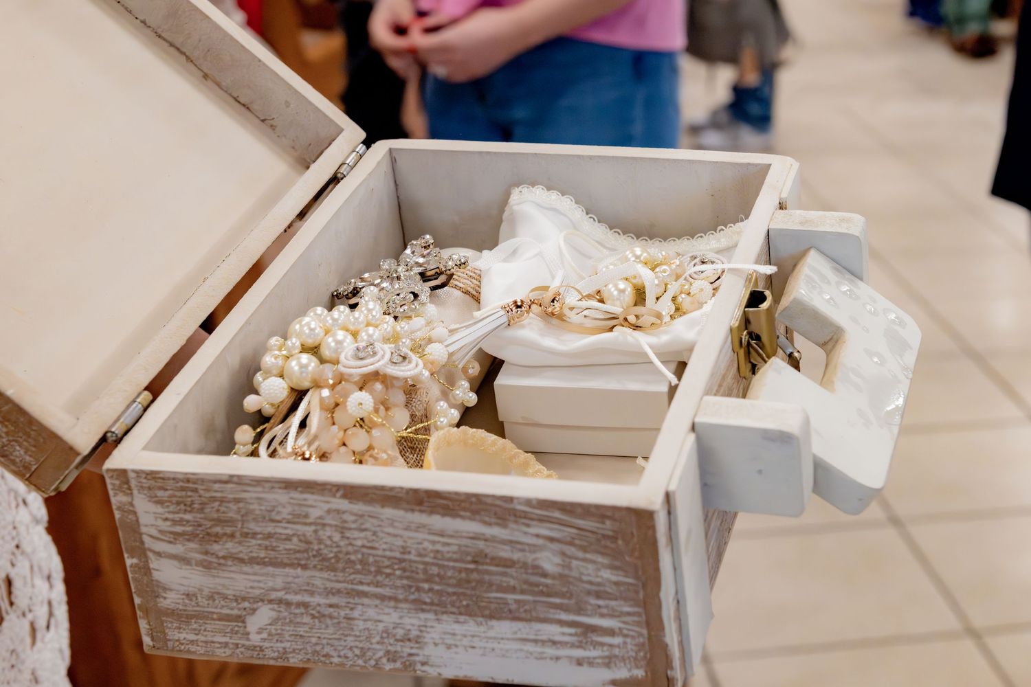 Rustic white wooden jewelry box filled with pearl accessories and vintage bridal trinkets at a wedding display.