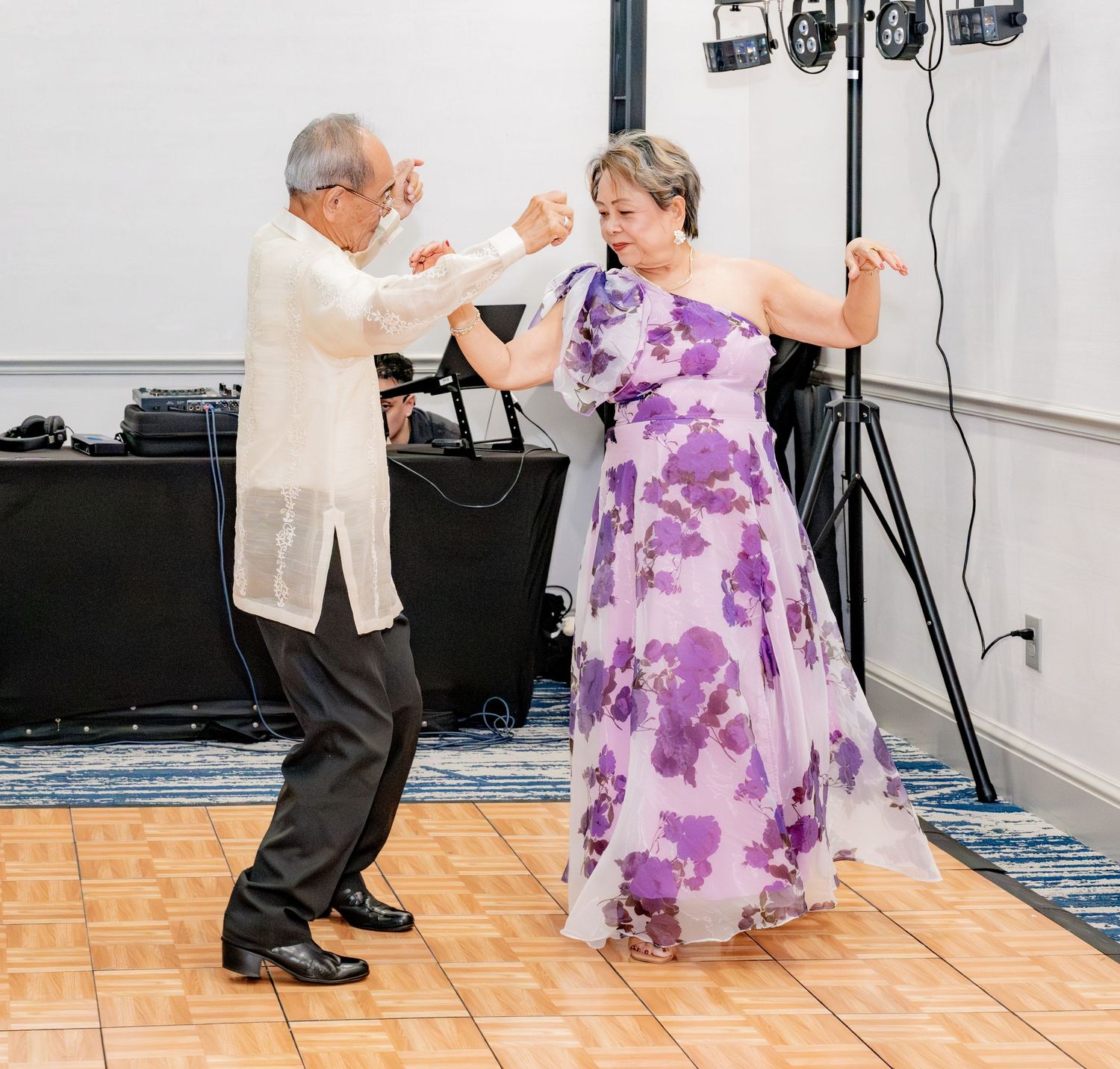 Elderly couple elegantly dancing together at a formal event on a wooden dance floor.