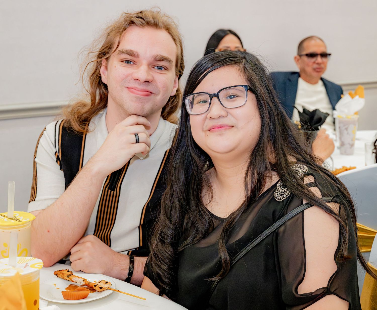 Young man and woman with glasses smiling together while seated at a birthday party dinner table.