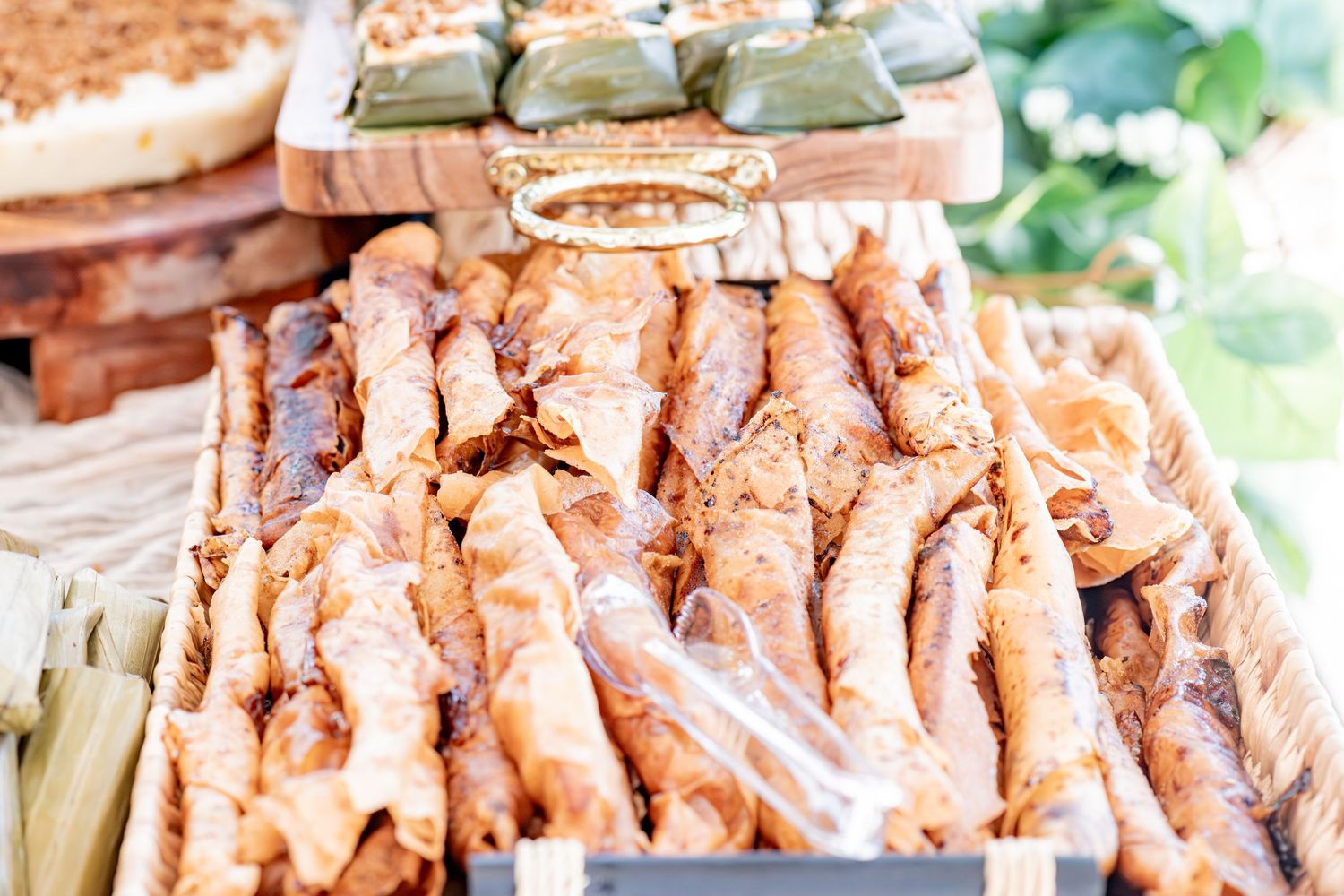 Golden fried spring rolls displayed in a wooden tray at a catered food buffet spread.