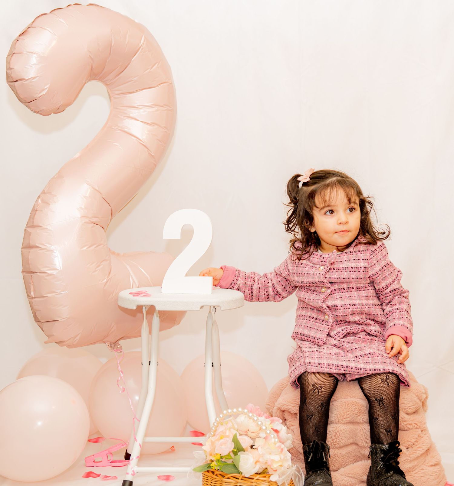 Toddler girl in pink dress celebrating 2nd birthday with number 2 balloon and white table decor.