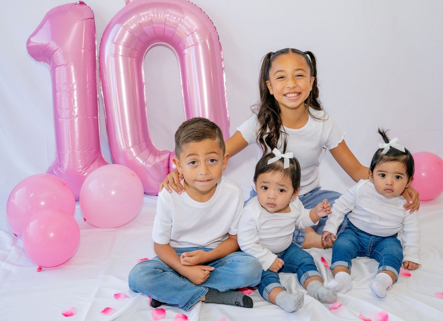 Four children pose together beside large pink number 10 balloon for birthday celebration.