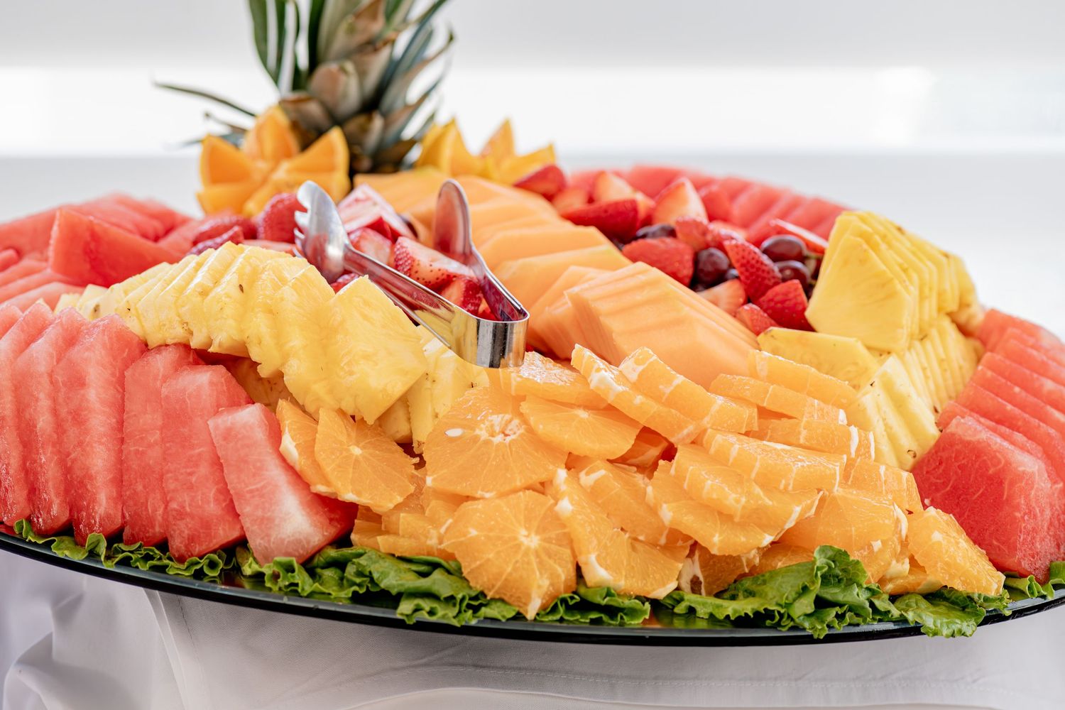 Colorful fresh fruit platter with watermelon, pineapple, cantaloupe and berries on a dark plate.