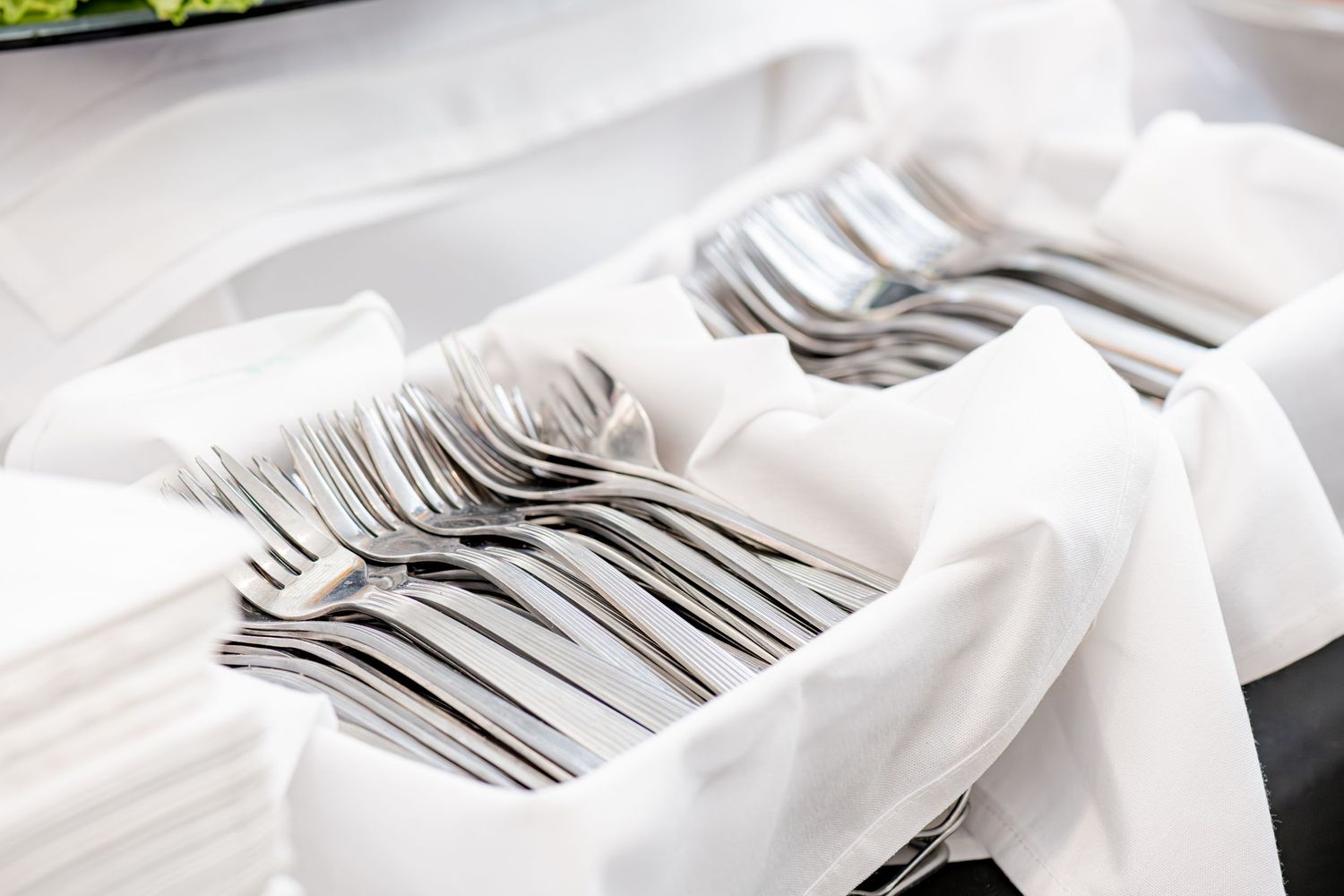 Stacks of clean silverware forks and spoons neatly arranged in white napkins in a wooden box.
