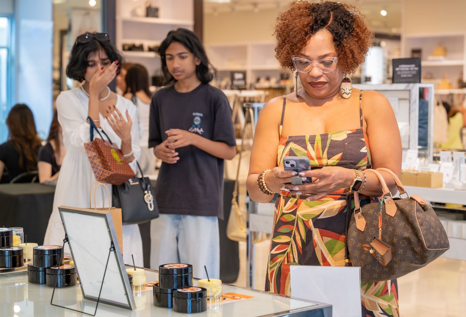 Woman in a floral dress browsing products on her phone at a luxury cosmetics store display.