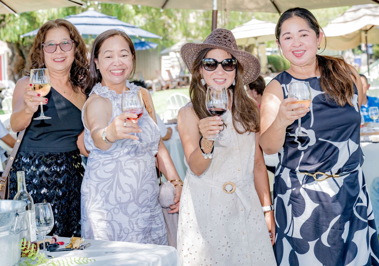 Four women toasting with wine glasses outdoors at a sunny garden party event.