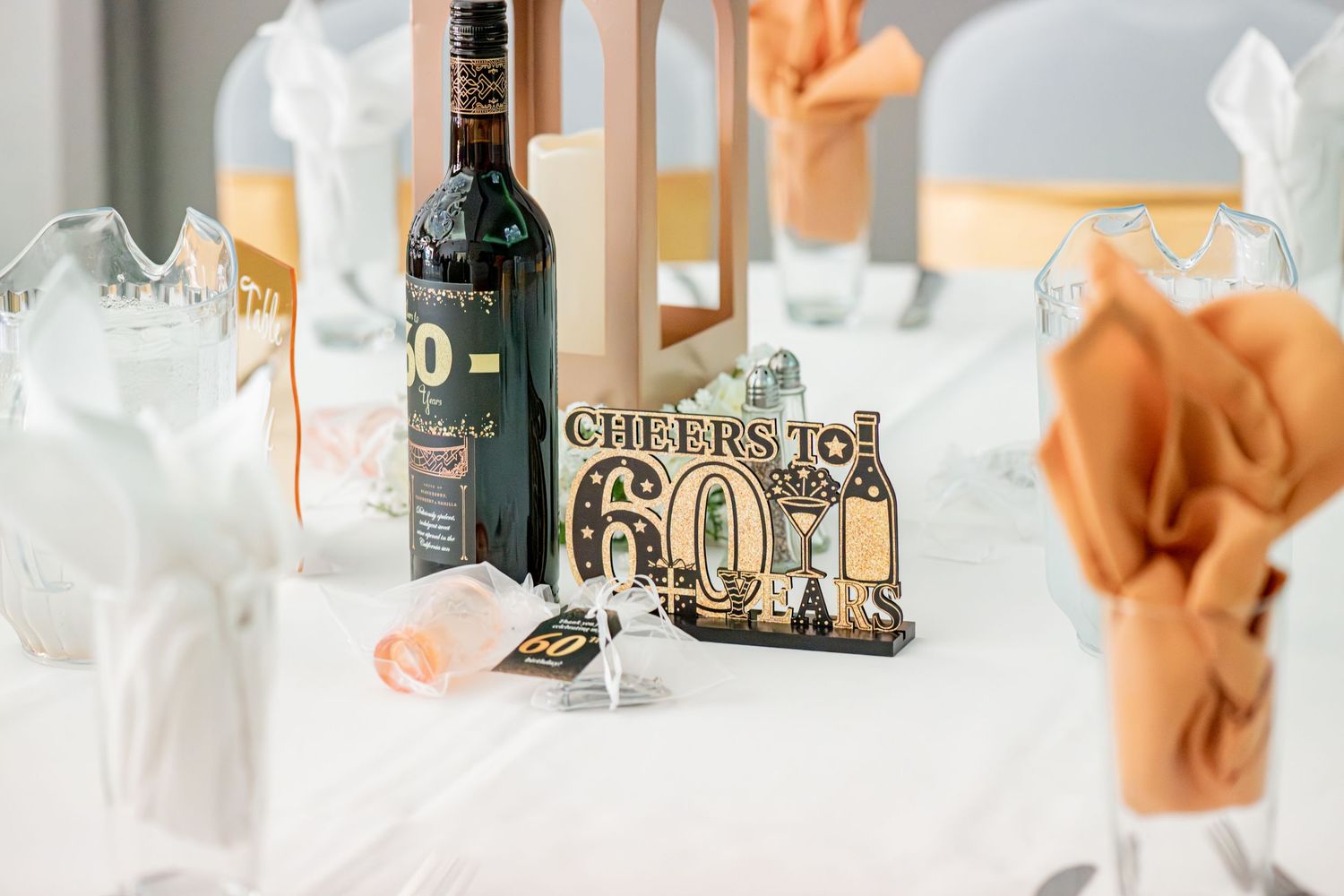 Cheers to 60 themed party table centerpiece with wine bottle and orange napkin decorations.