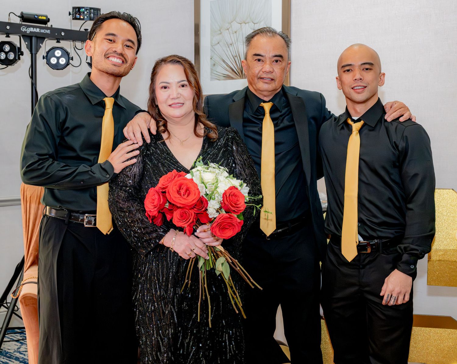 Family of four posing with red roses at a formal black and gold themed party.