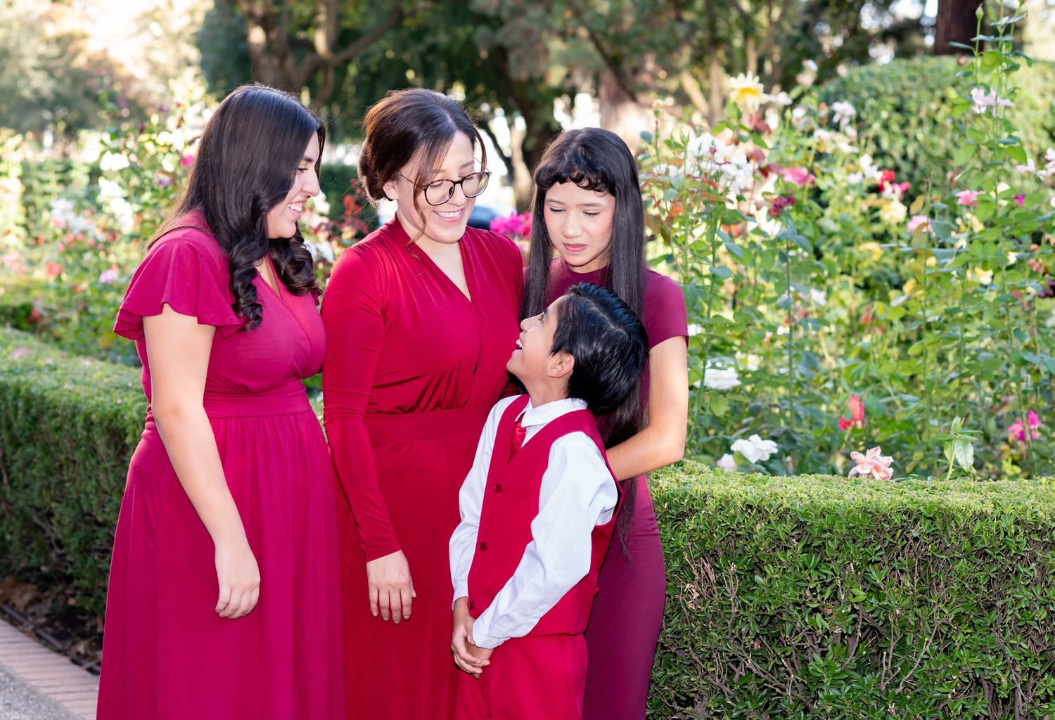 Family of four in red outfits sharing a joyful moment together in a rose garden.