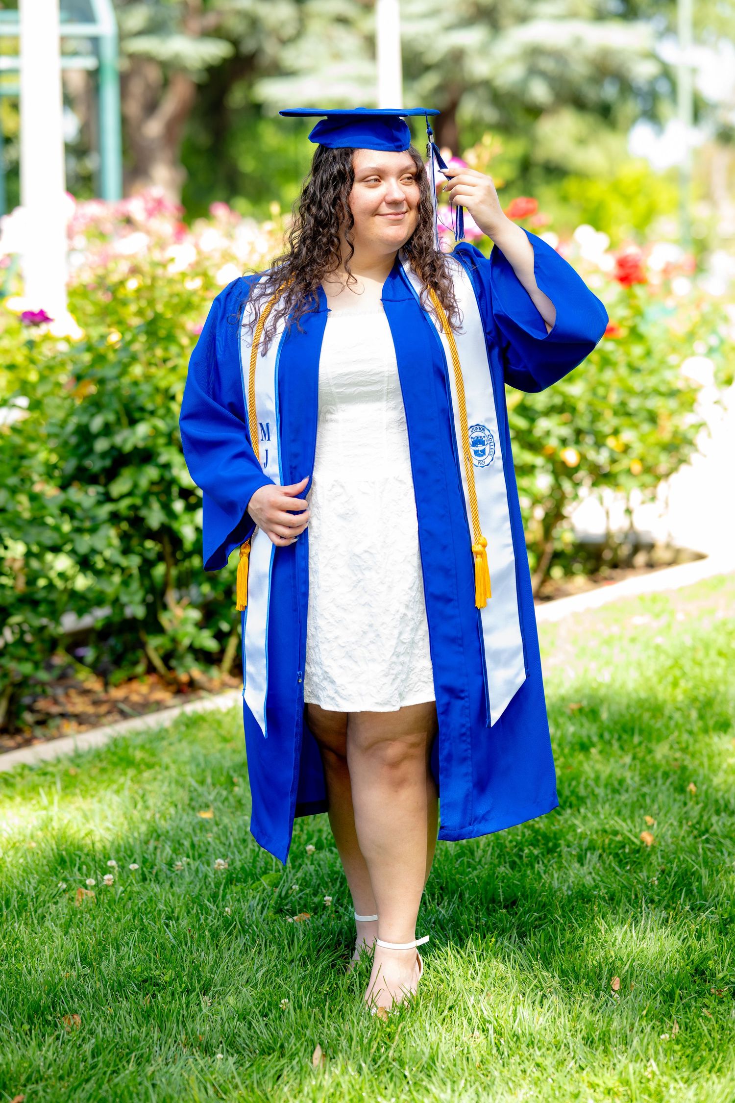 Proud graduate in blue cap and gown holds diploma while standing on green lawn.