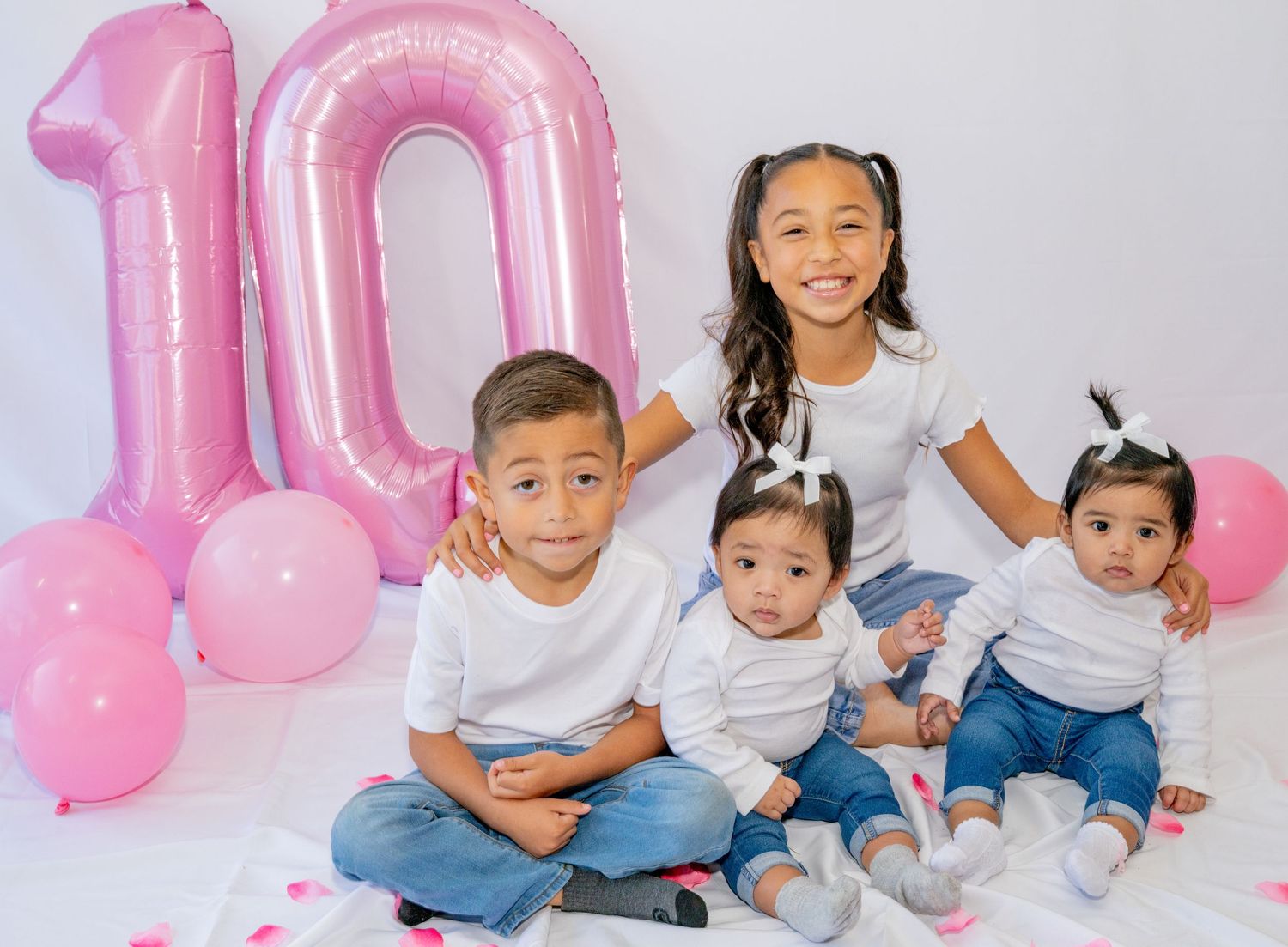 Four siblings smile together in front of pink number 10 balloons at a birthday photo session.