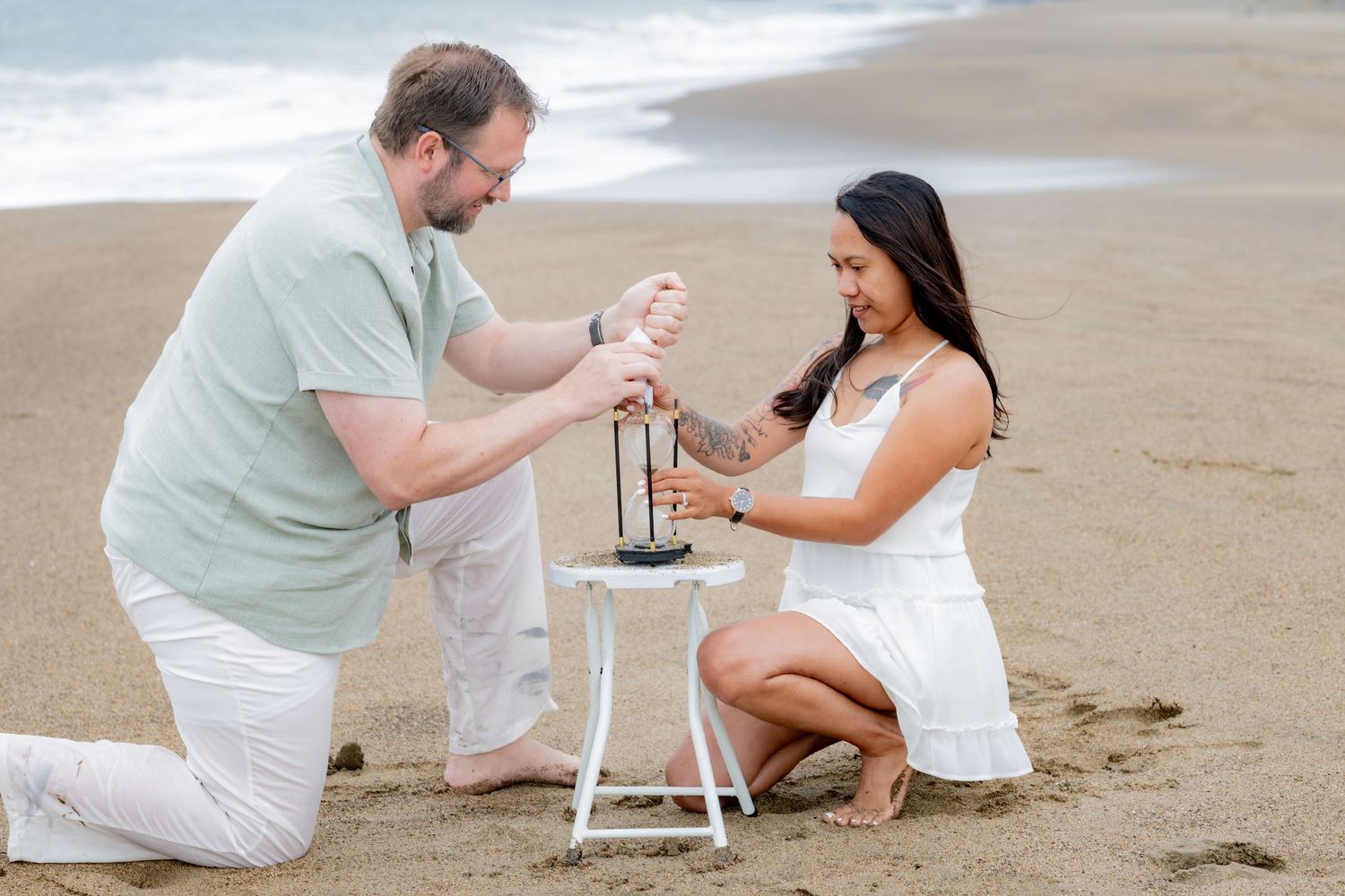 Man and woman kneeling on sandy beach near Golden Gate Bridge, lighting a lantern together.