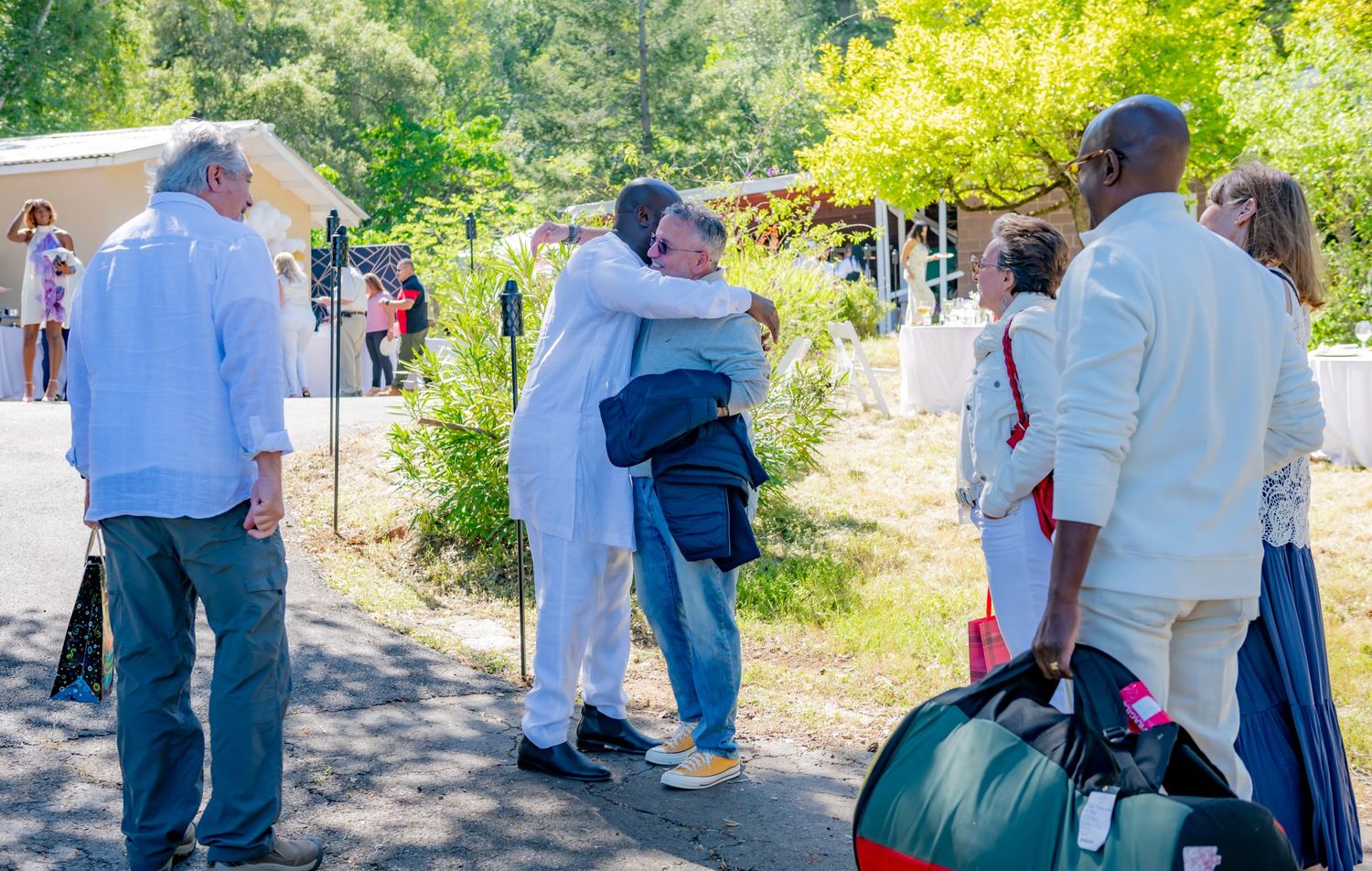 Guests greeting each other with hugs at an outdoor gathering.