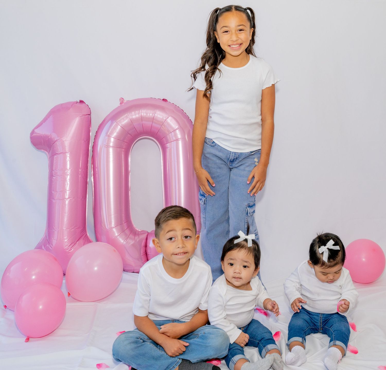 Four children pose with pink number 10 balloons for a 10th birthday celebration photo shoot.