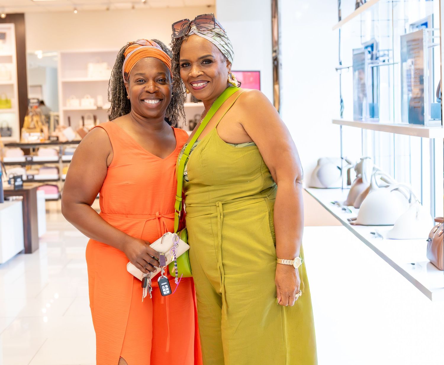 Two women smiling together in colorful orange and green outfits inside a store.