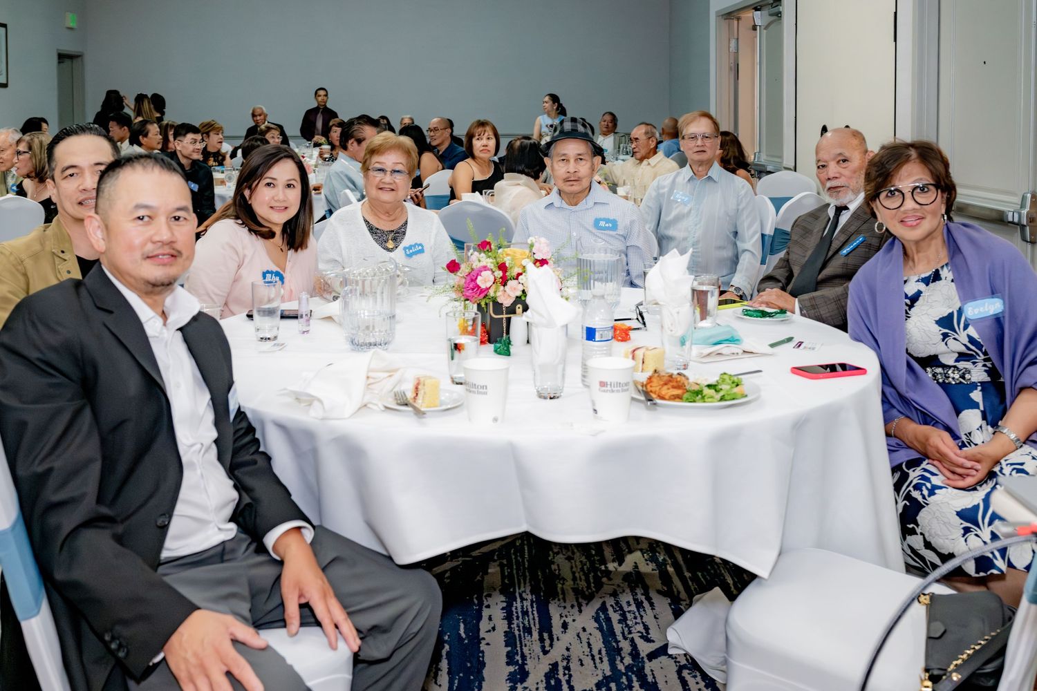Group of smiling guests seated at a round banquet table during a formal indoor event.