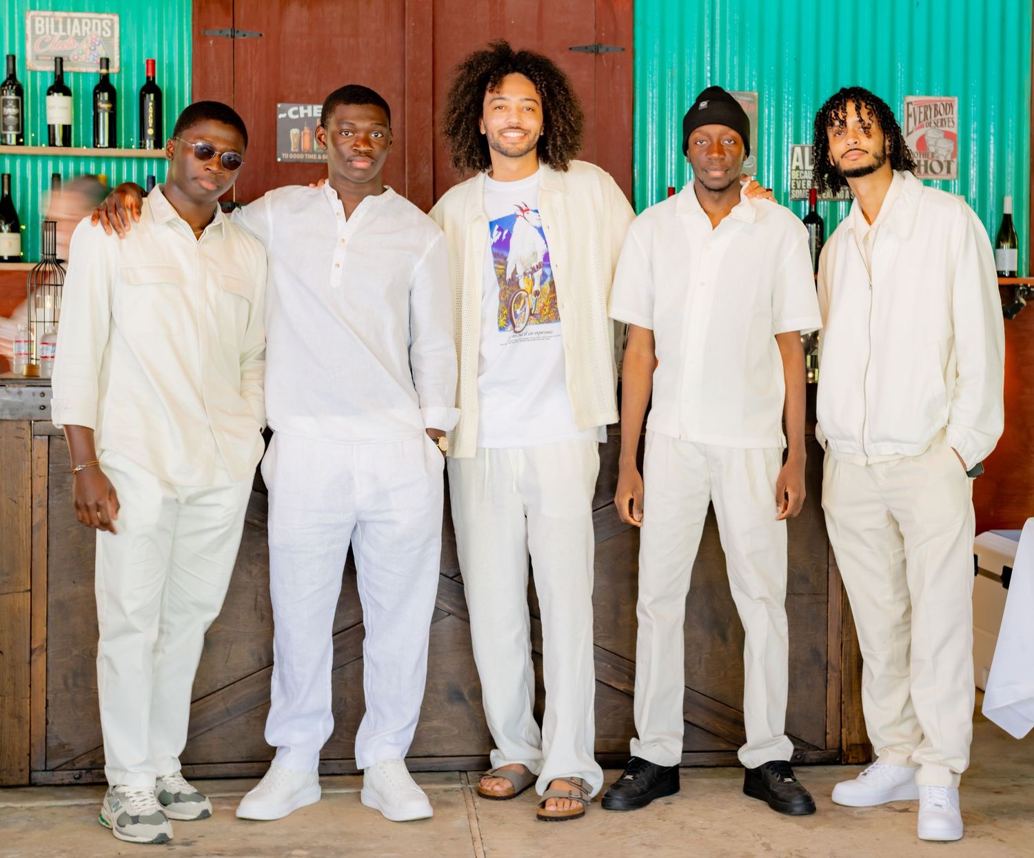 Five young men posing together in white outfits at an indoor venue.