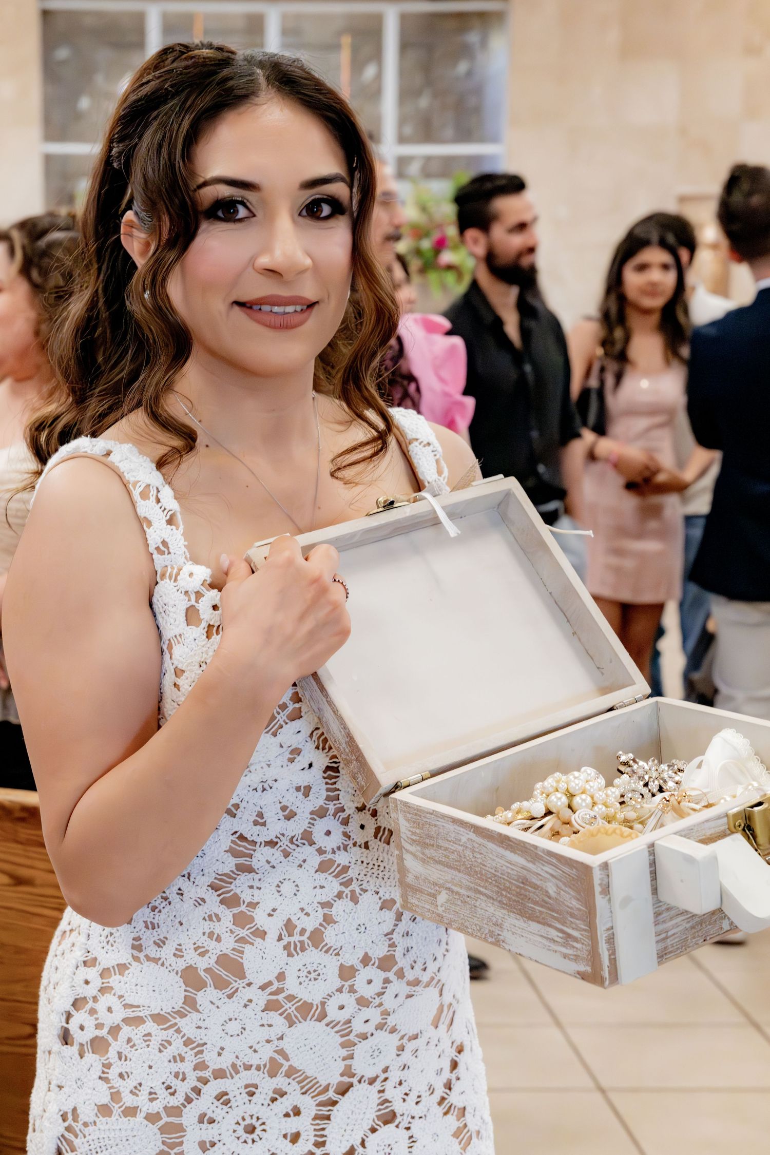 Young woman in white lace dress holds wooden box with baptism accessories at celebration.