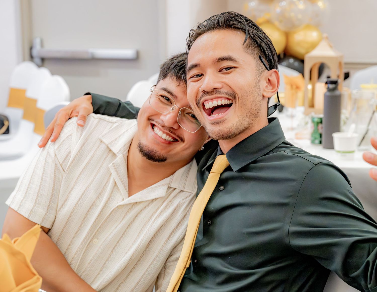 Two young men laughing and embracing at a celebratory party.