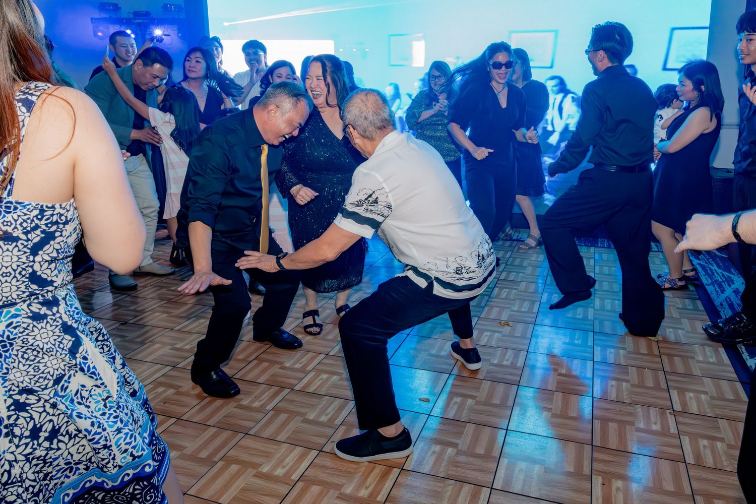 Two men doing low dance moves on a dance floor at a lively indoor celebration.