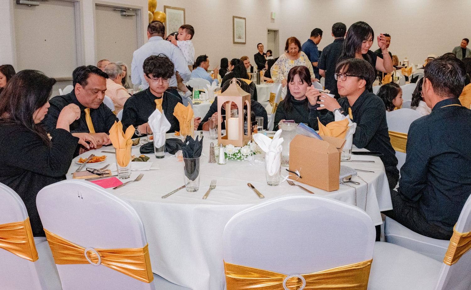 Guests seated at round tables with gold sashes enjoying dinner at an elegant birthday celebration.