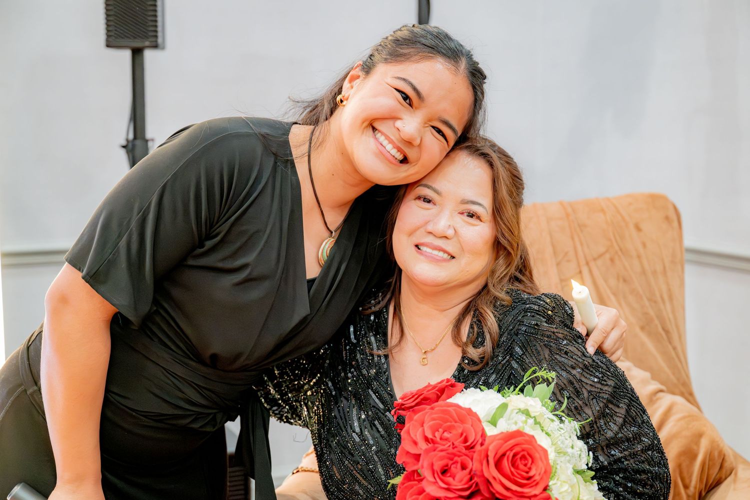 Two women smiling together at a party, one holding a bouquet of red and white roses.