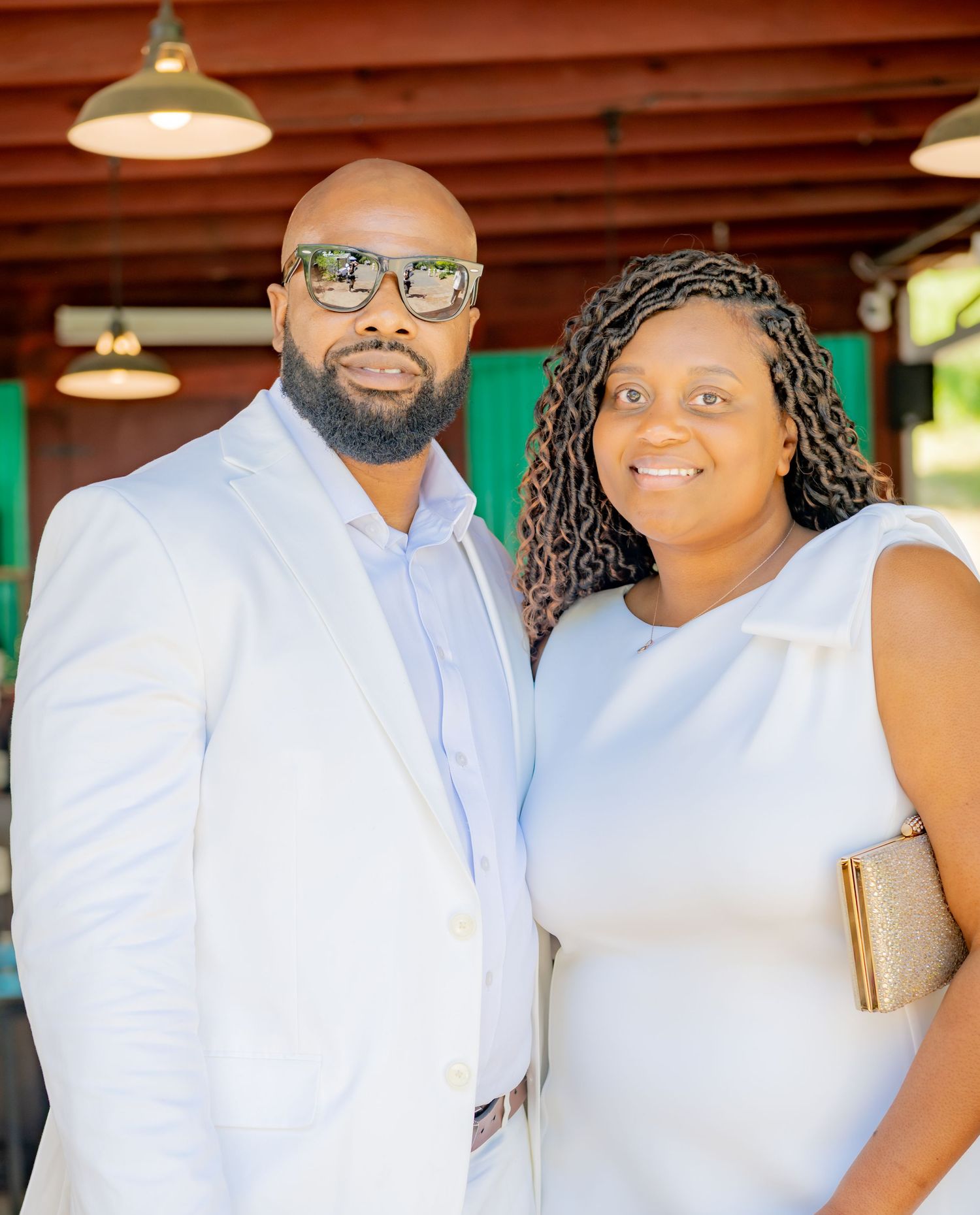 Couple posing together indoors at an elegant event, man in white blazer with sunglasses.
