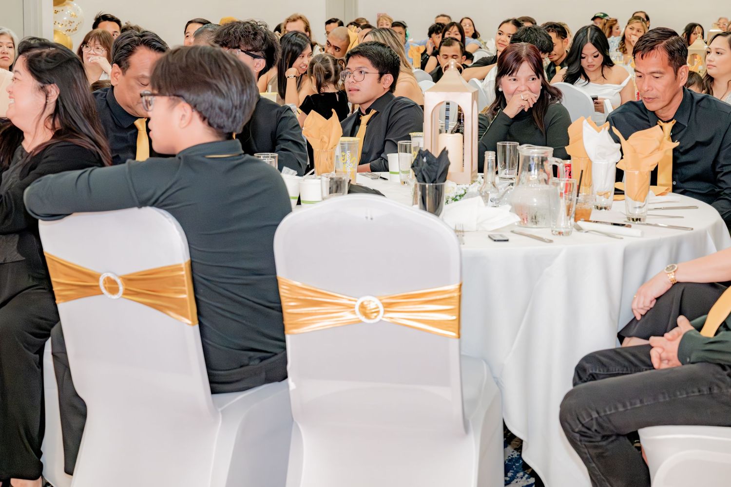 Guests seated at elegantly decorated round tables with gold accents at a formal event.