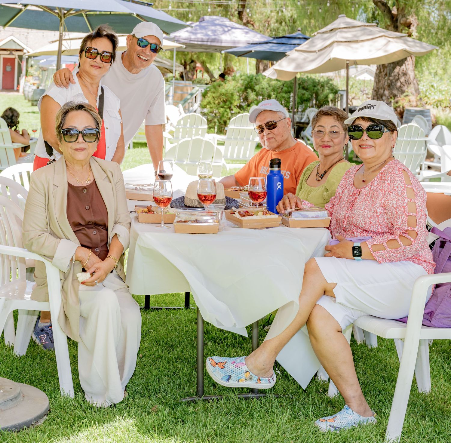 Group of friends enjoying an outdoor lunch at a table with umbrellas on a sunny day.