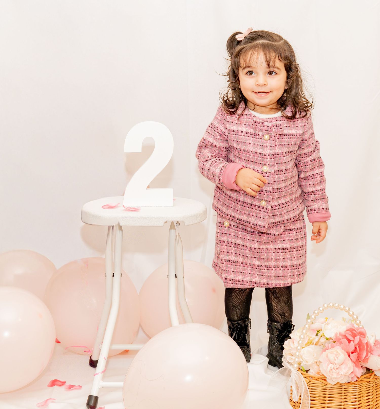 Toddler girl in pink tweed dress celebrating 2nd birthday with balloons and floral decorations.