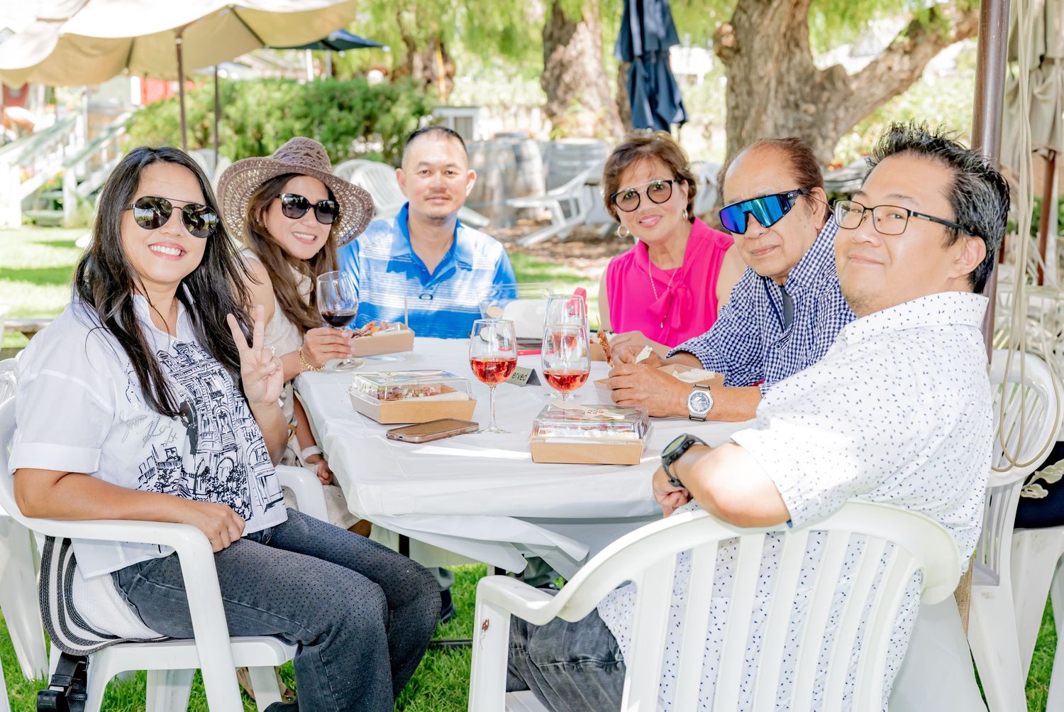 Group of friends enjoying wine and food at an outdoor table on a sunny day.
