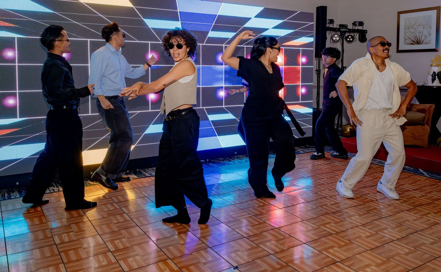 Group of people performing a coordinated dance routine at a party with LED backdrop.
