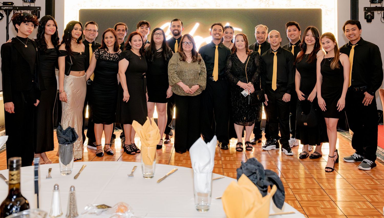 Large group of formally dressed guests in black and gold posing together at a birthday celebration.