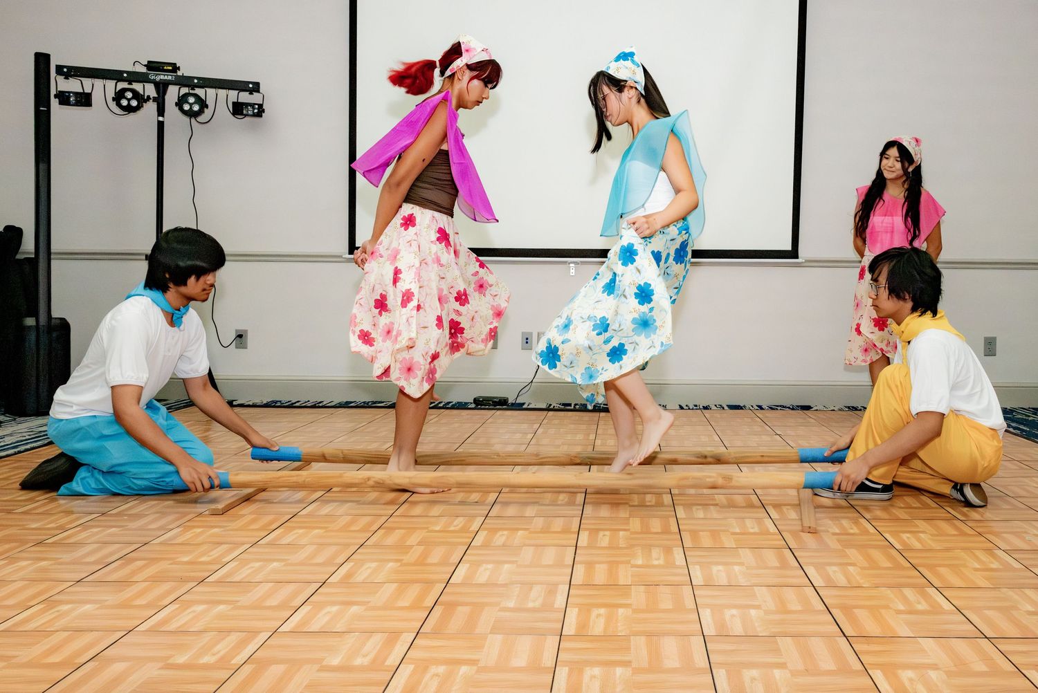 Young performers in colorful floral dresses dance during a traditional cultural stage performance.