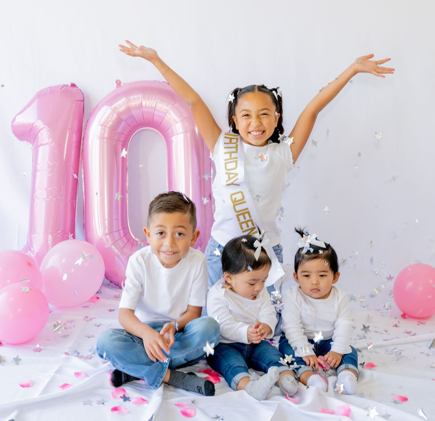 Four children celebrate 10th birthday with confetti and pink balloons in a white studio setting.
