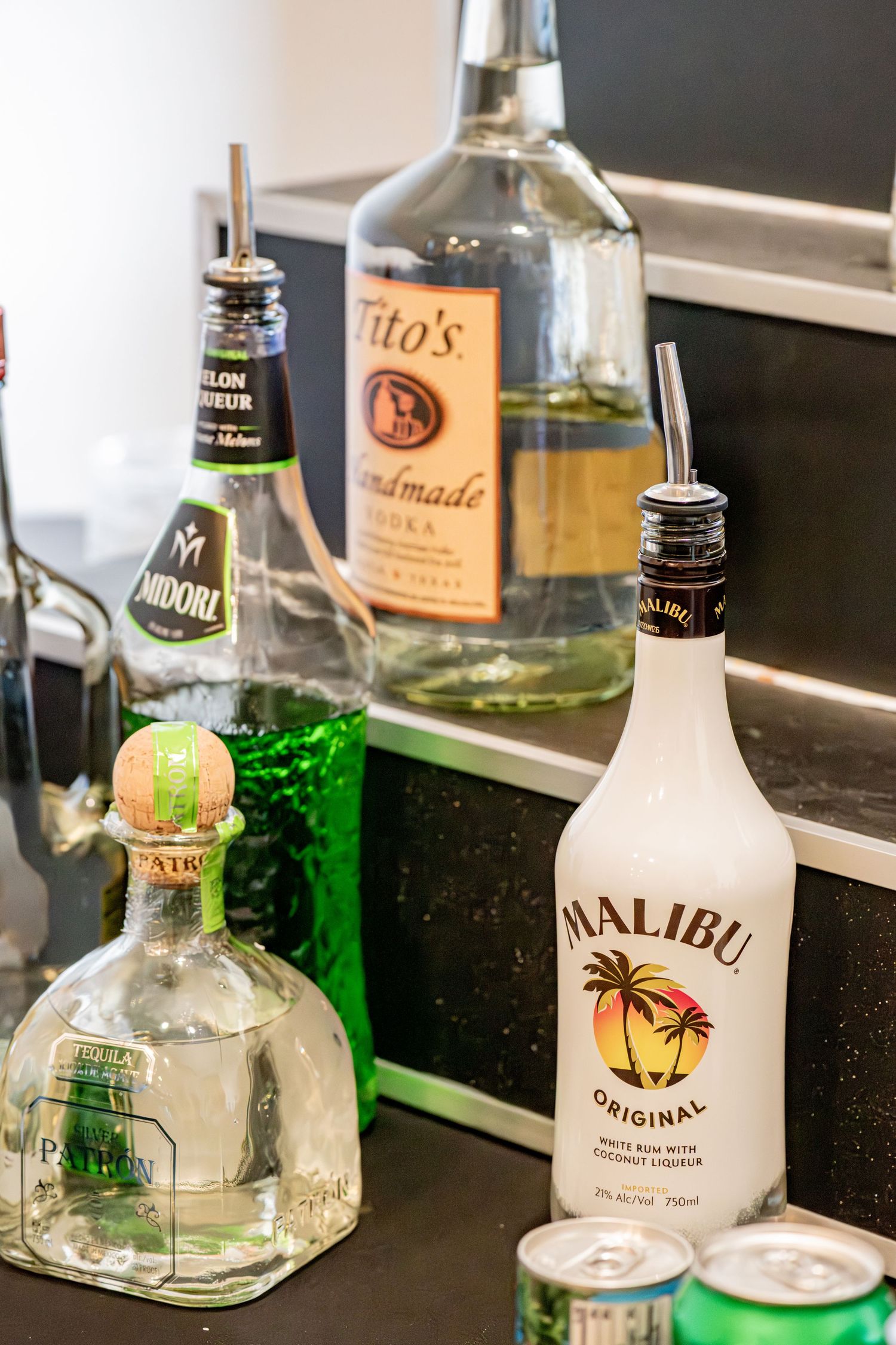 Assorted liquor bottles including Malibu, Patron, Titos vodka and Midori on a bar counter.