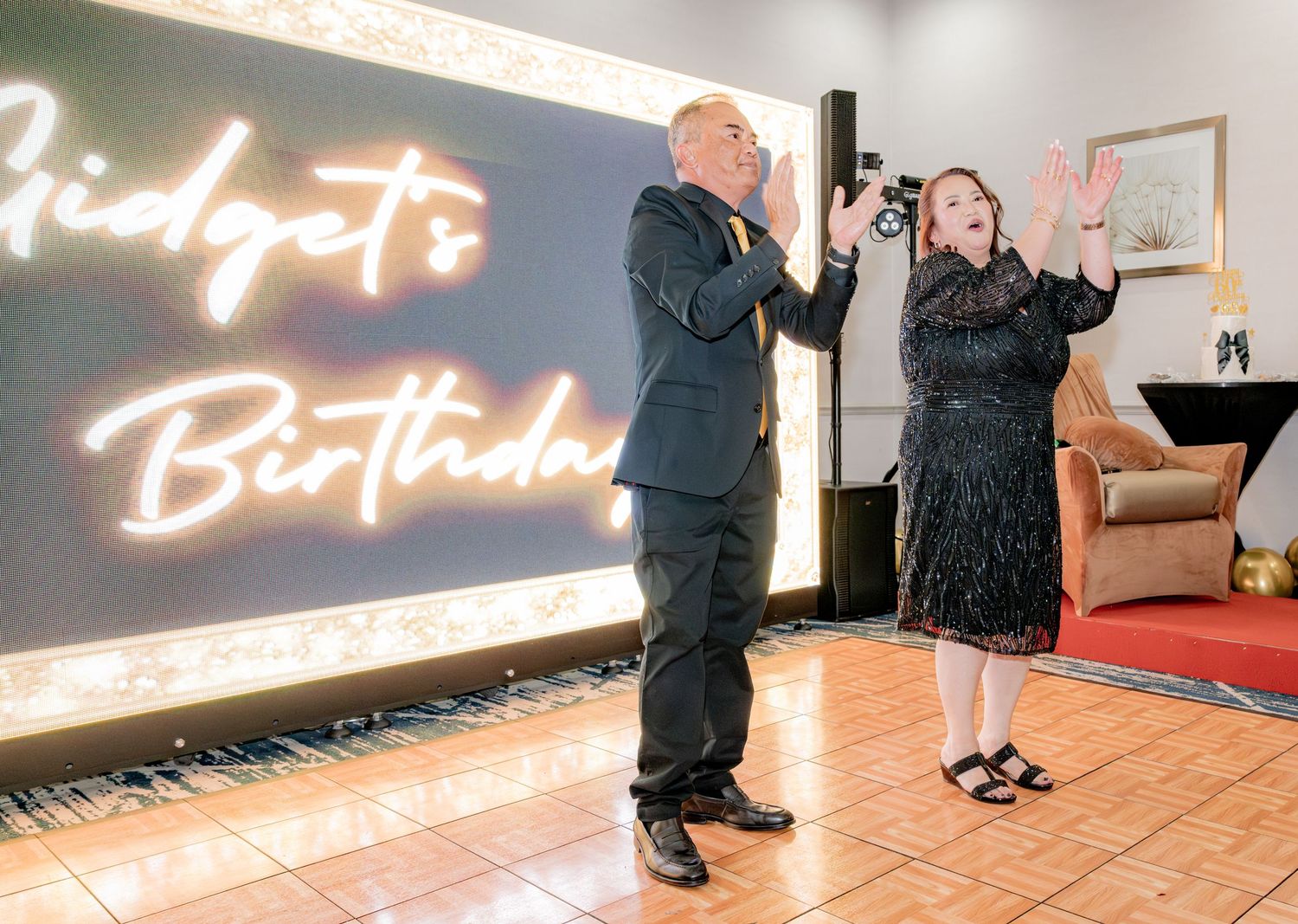 Man and woman celebrate at Gidget's Birthday party in front of glowing neon sign.