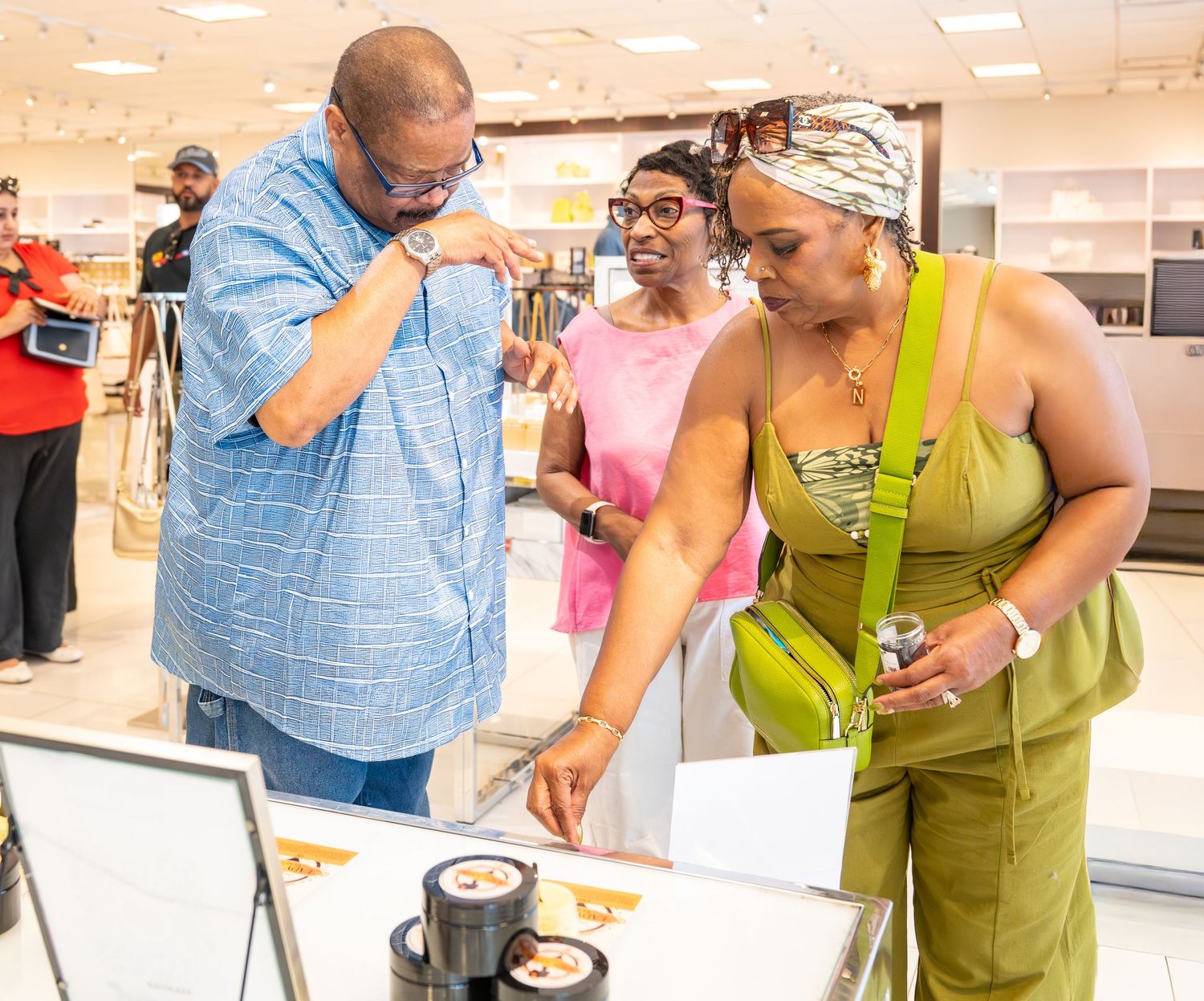 Three people examine products in a display case at a retail store.
