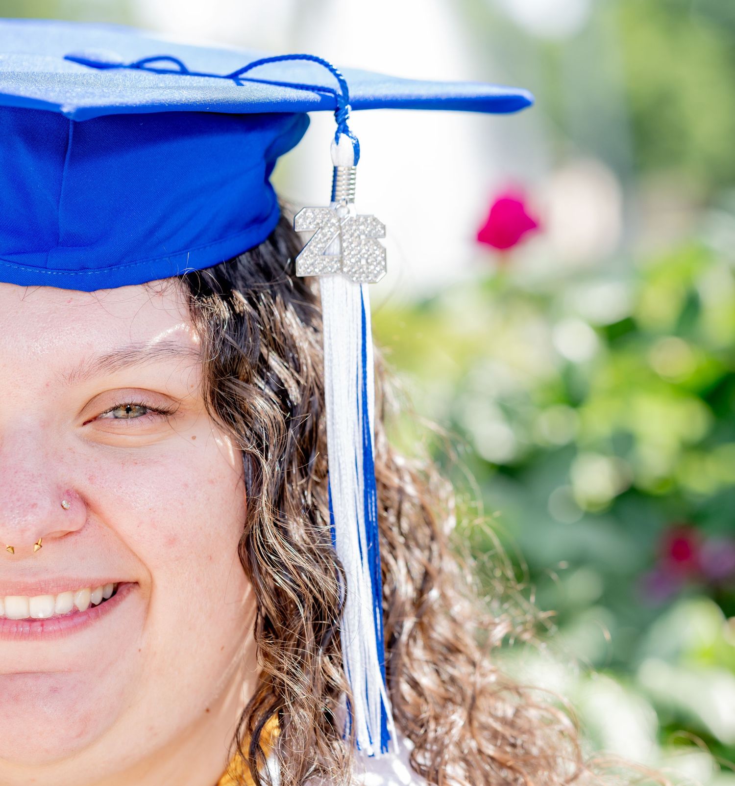Close-up of smiling female graduate wearing blue mortarboard cap with decorative tassel charm.