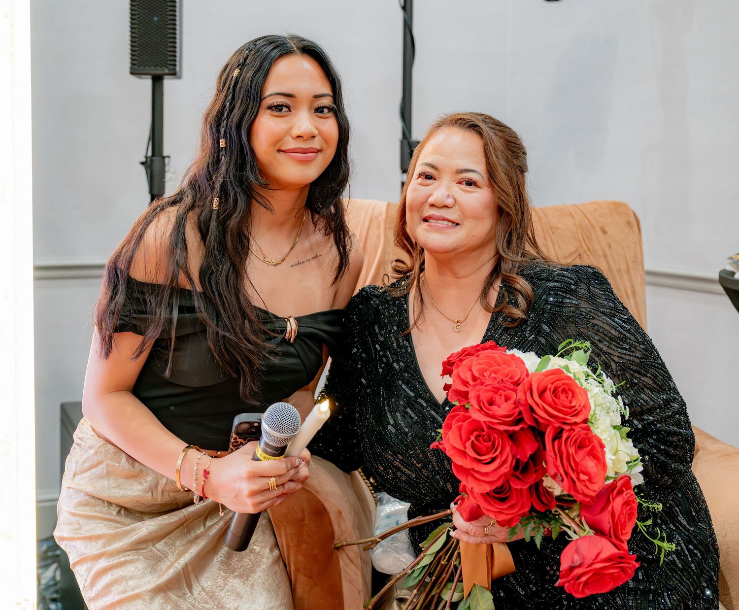 Young woman and older woman posing together with red roses at a 60th birthday party.