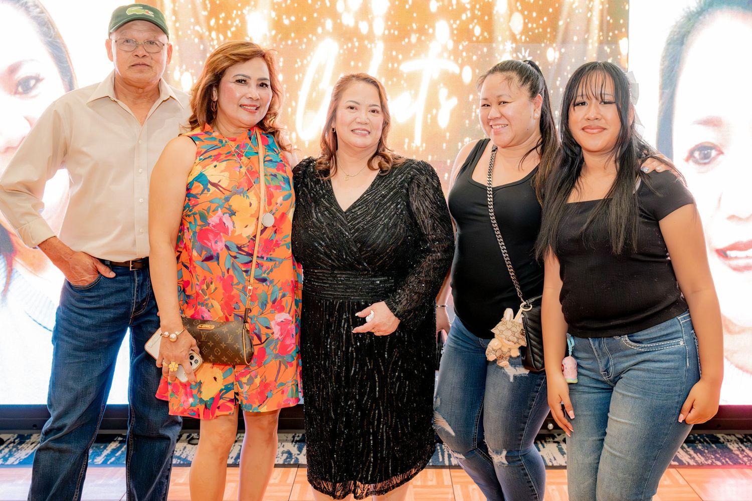 Five guests smiling together at a festive celebration event with colorful backdrop.
