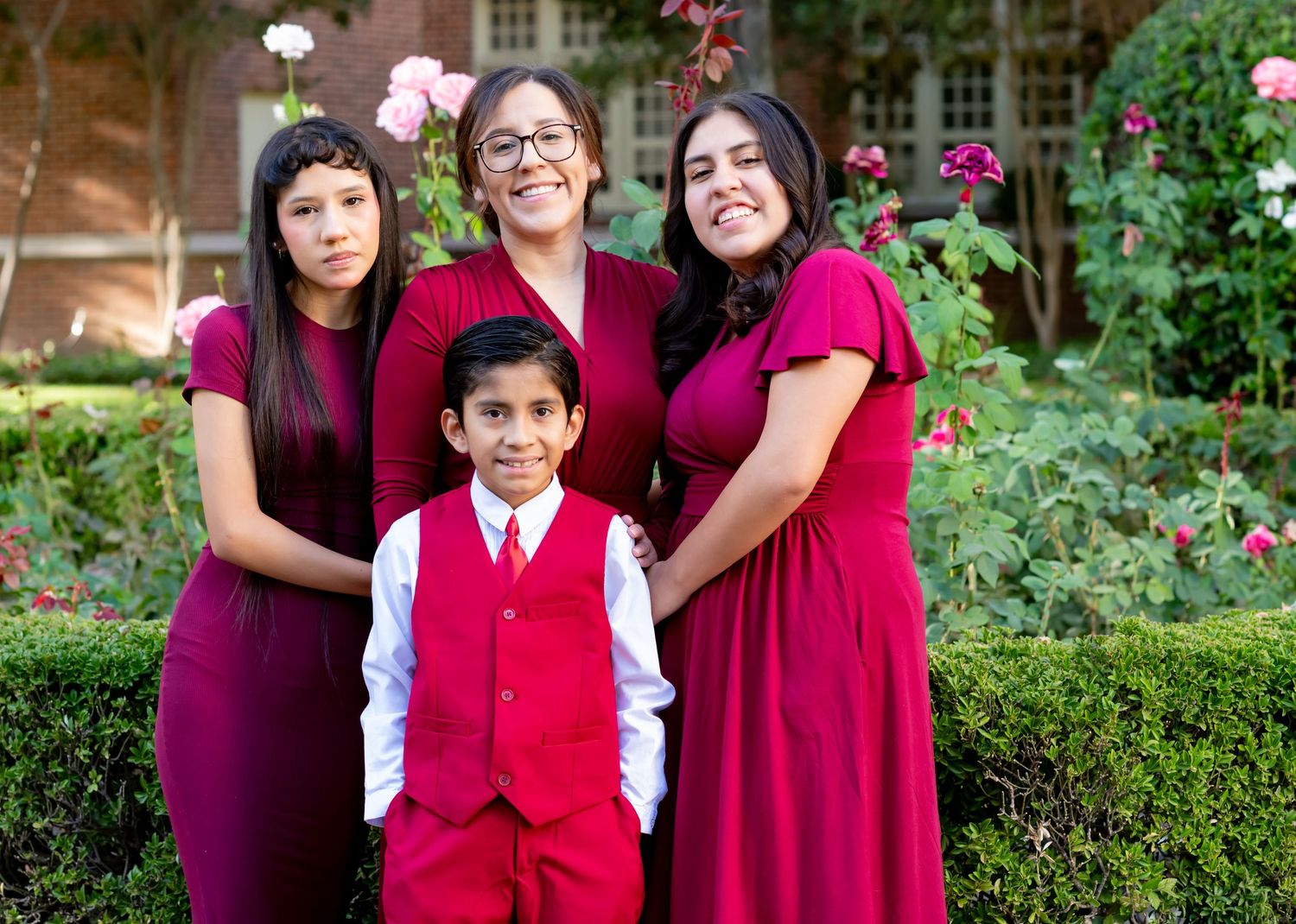 Family of four in matching burgundy outfits posing together in a garden with roses.
