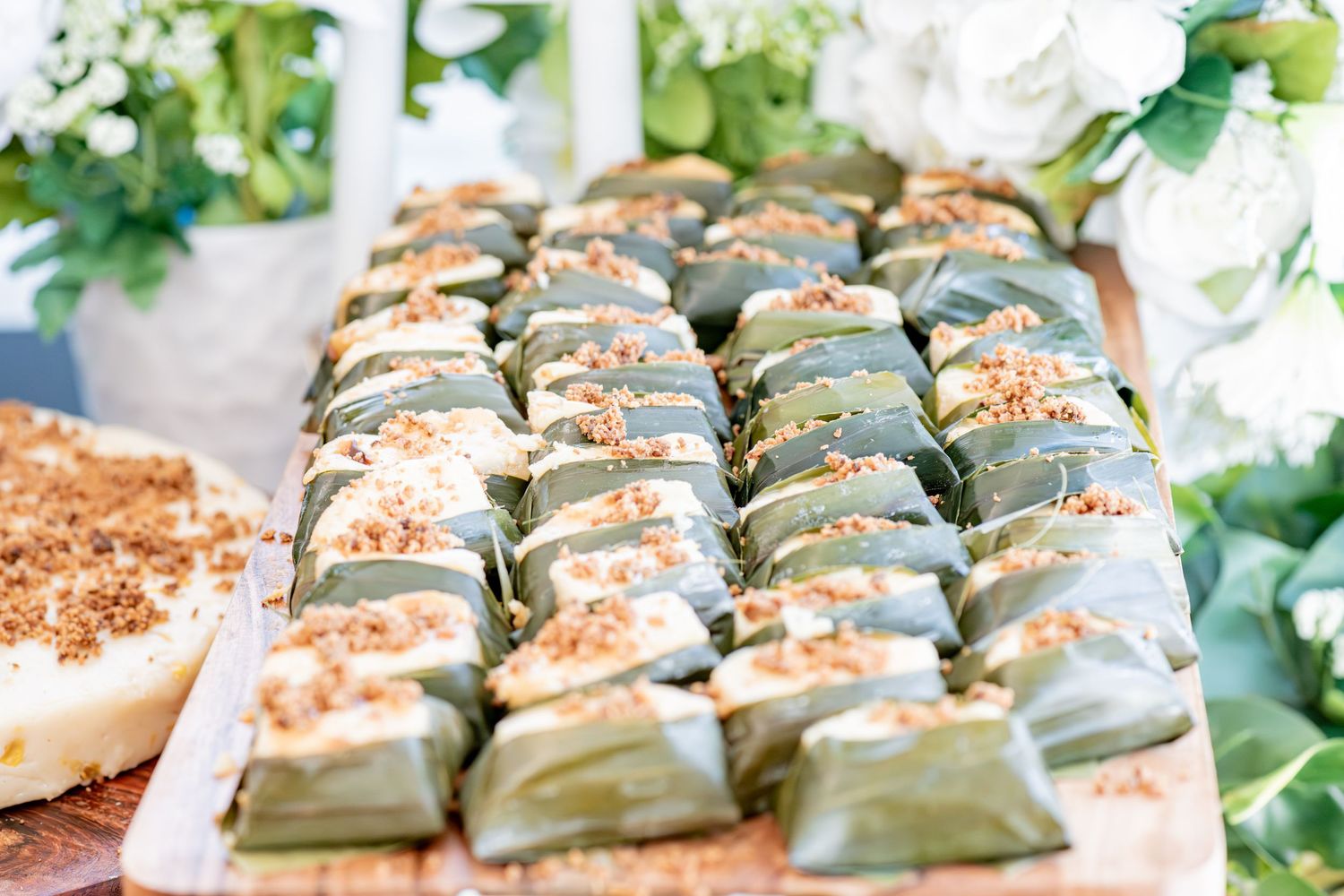 Traditional green banana leaf wrapped rice parcels topped with toasted coconut on a wooden board.