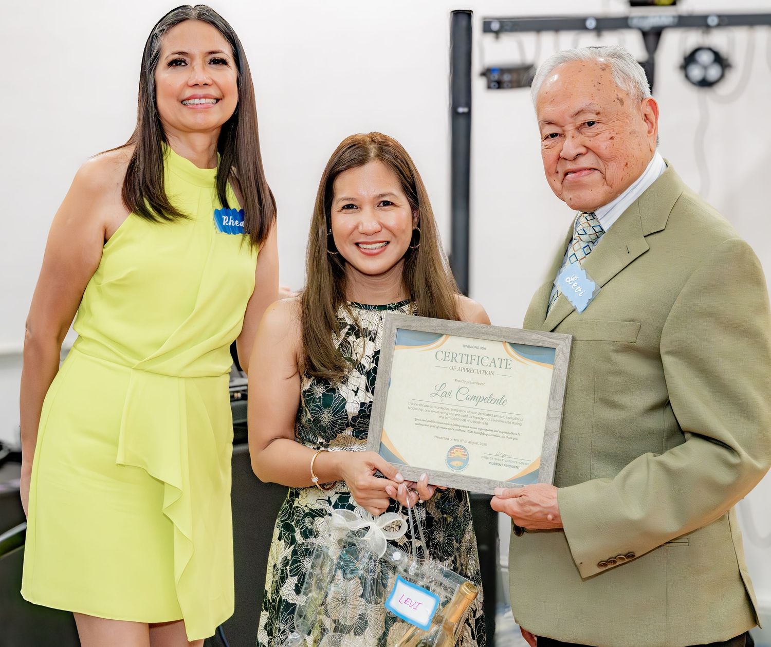 Three people pose together at an award ceremony, with a woman proudly holding a certificate of achievement.