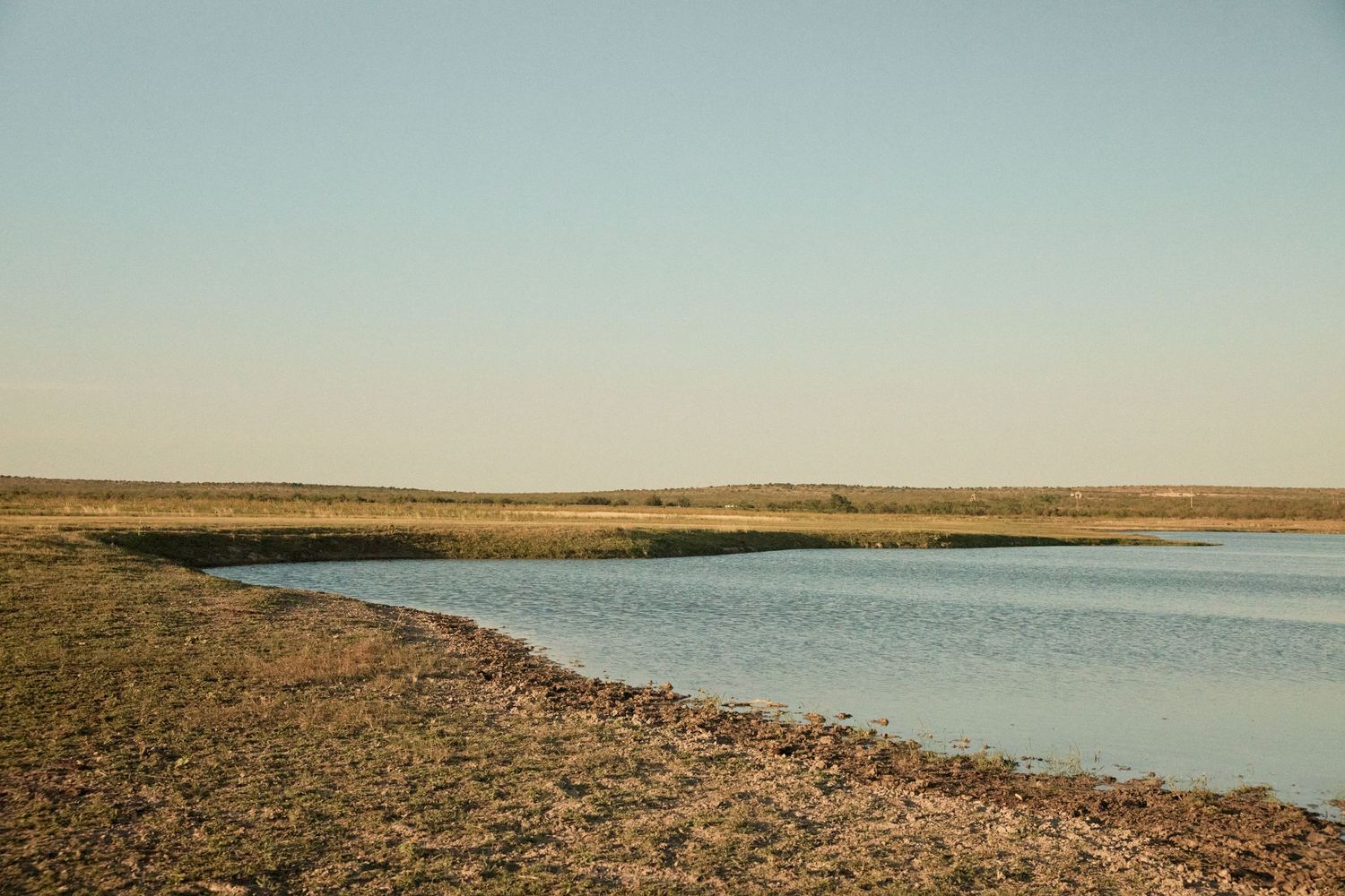 A serene lake landscape with golden grasslands and distant hills under a clear sky.