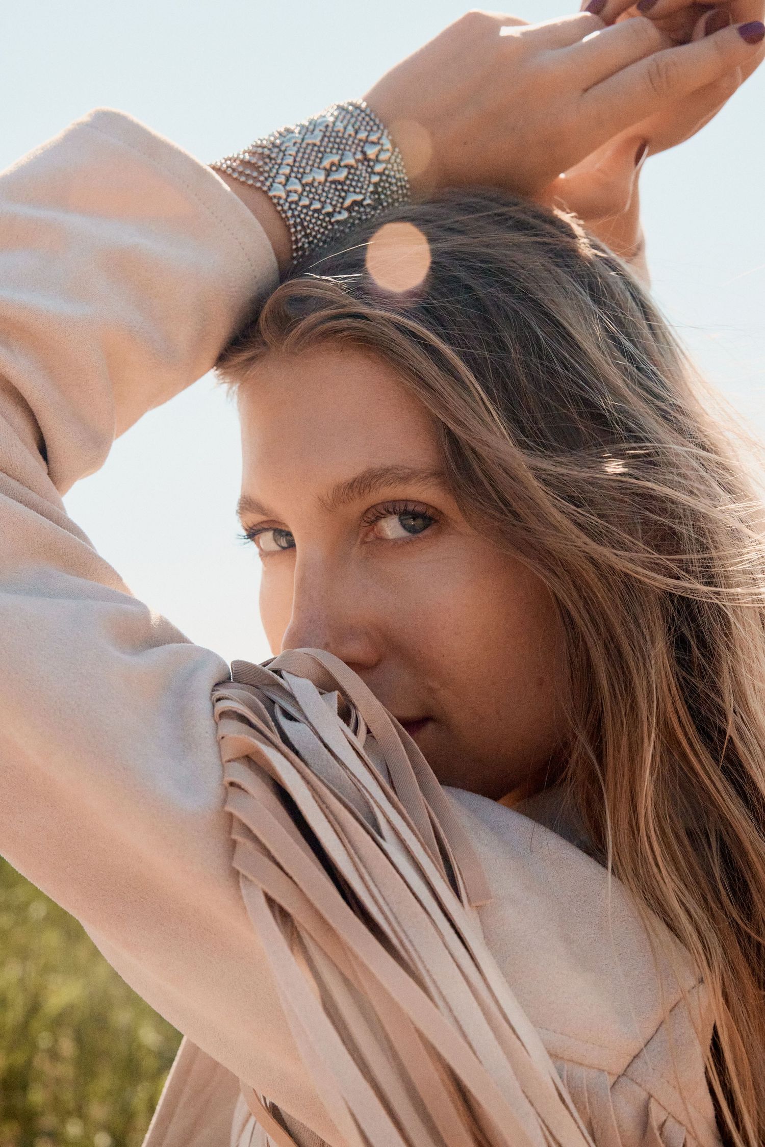 Close-up of woman with arms raised wearing a silver beaded cuff bracelet in sunlight.