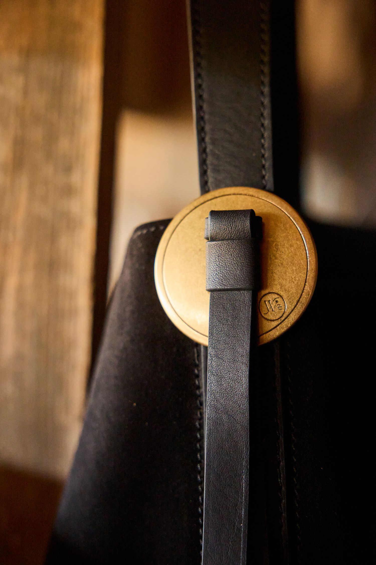 Close-up of a black leather bag with a gold circular buckle closure detail.